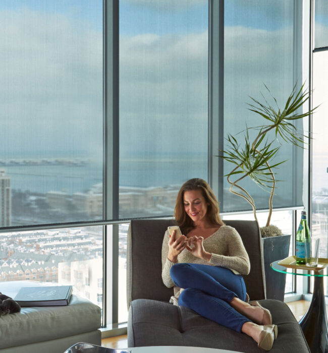Person relaxing in front of floor to ceiling penthouse windows, with partially drawn roller blinds